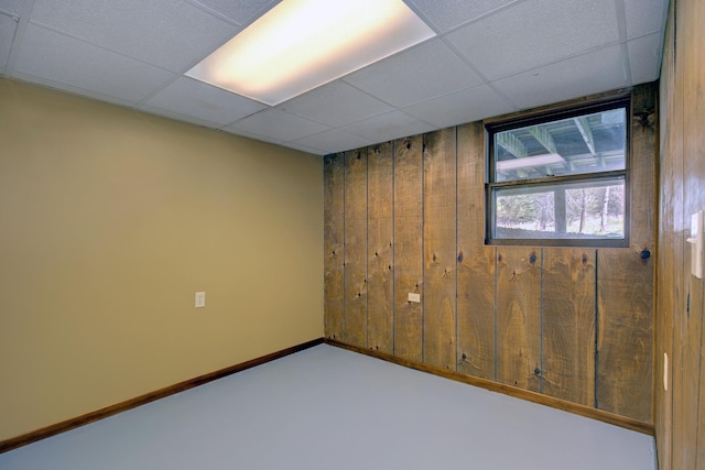 basement with carpet flooring, a drop ceiling, baseboards, and wooden walls
