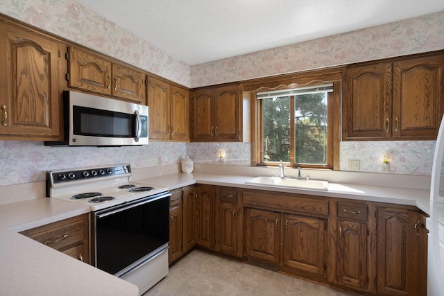 kitchen featuring stainless steel microwave, electric range, a sink, wallpapered walls, and light countertops