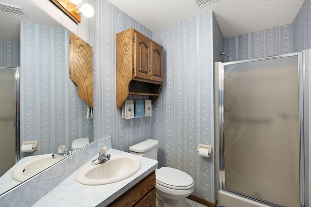 full bathroom with wallpapered walls, a stall shower, toilet, vanity, and a textured ceiling