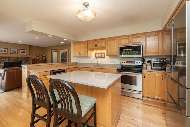 kitchen with stainless steel appliances, a sink, a peninsula, light wood finished floors, and recessed lighting
