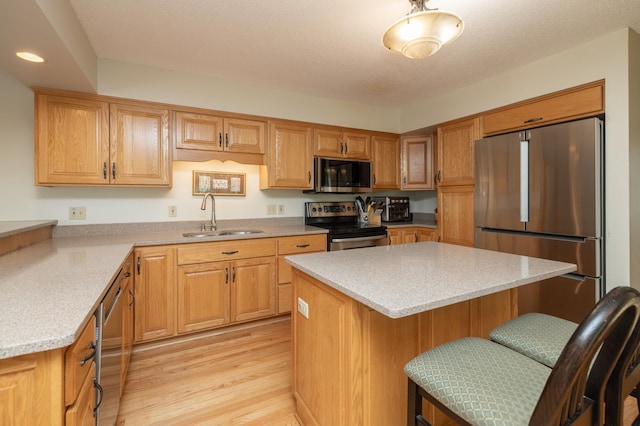 kitchen featuring stainless steel appliances, a sink, a kitchen bar, recessed lighting, and light wood-style floors
