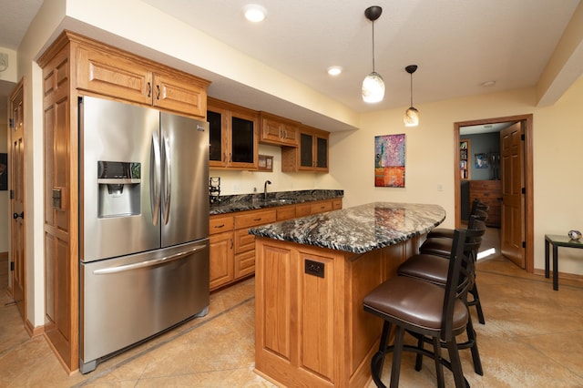 kitchen featuring stainless steel refrigerator with ice dispenser, a center island, a breakfast bar, glass insert cabinets, and decorative light fixtures