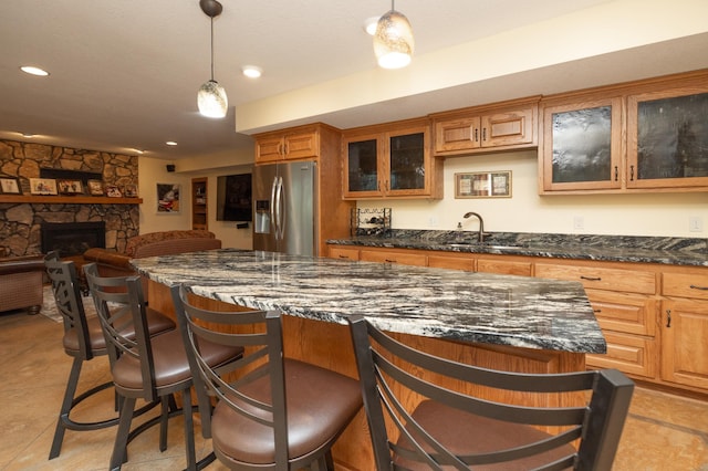 kitchen with stainless steel fridge, a sink, a breakfast bar area, brown cabinets, and dark stone countertops