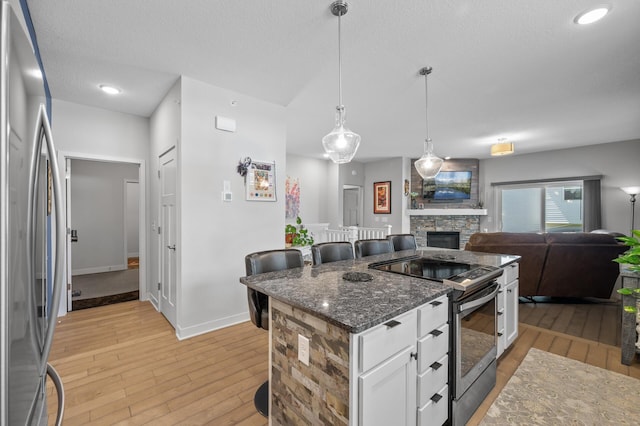 11062 16th St NE, Saint Michael, MN 55376 - kitchen featuring appliances with stainless steel finishes, light wood-type flooring, a stone fireplace, white cabinets, and dark stone counters
