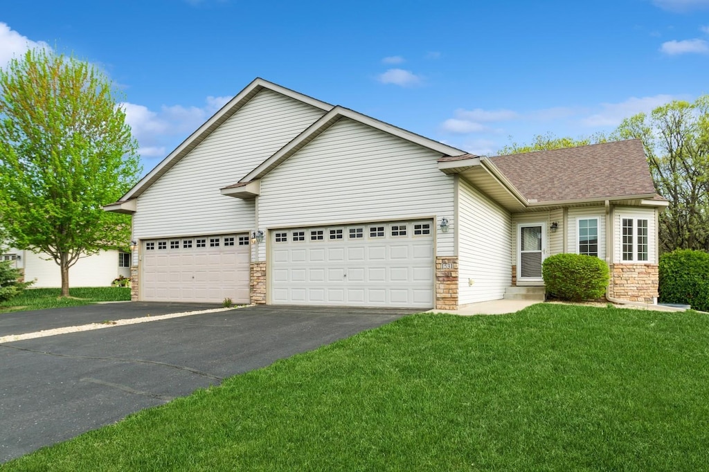 view of front of home with asphalt driveway, stone siding, a garage, a front lawn, and a shingled roof