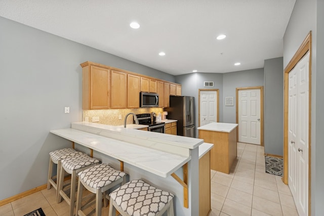 12245 Urbank St NE Unit E, Blaine, MN 55449 - kitchen featuring appliances with stainless steel finishes, a center island, light tile patterned floors, tasteful backsplash, and a peninsula