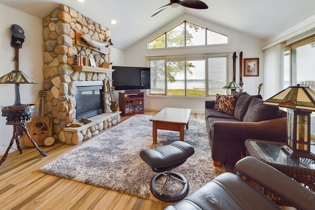 living area featuring wood finished floors, vaulted ceiling, a ceiling fan, a stone fireplace, and recessed lighting