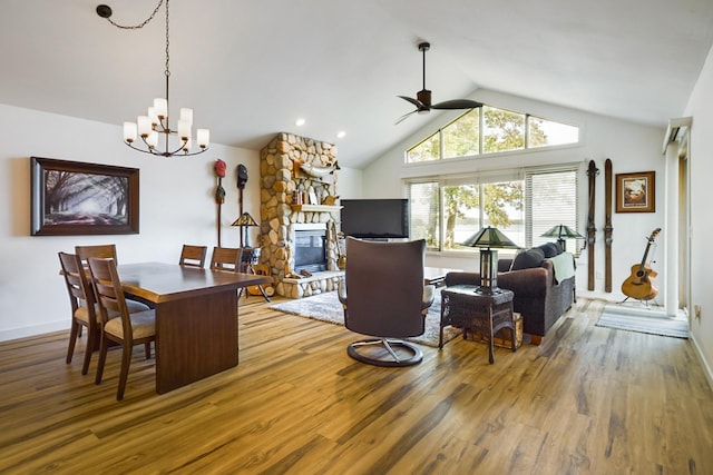 dining room with wood finished floors, lofted ceiling, a fireplace, ceiling fan, and a chandelier