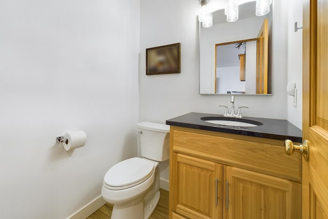 half bathroom featuring toilet, vanity, wood finished floors, and baseboards