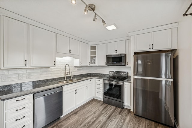 kitchen with white cabinetry, stainless steel appliances, dark stone counters, and a sink