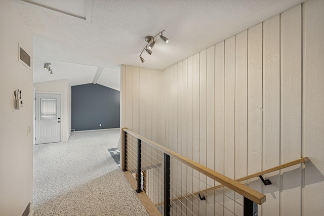 hallway with carpet, track lighting, a textured ceiling, visible vents, and lofted ceiling