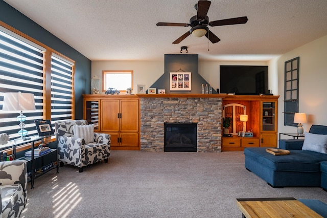 carpeted living room with a textured ceiling, a ceiling fan, and a stone fireplace
