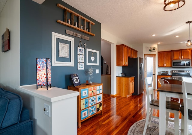 kitchen with appliances with stainless steel finishes, dark wood-type flooring, a textured ceiling, brown cabinets, and recessed lighting
