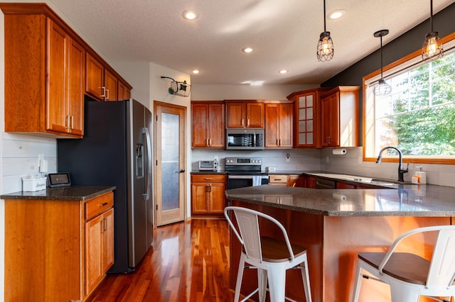 kitchen with appliances with stainless steel finishes, a breakfast bar, a peninsula, brown cabinets, and dark wood-style floors