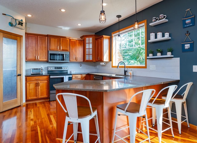 kitchen featuring stainless steel appliances, a sink, brown cabinetry, a kitchen breakfast bar, and light wood-style floors