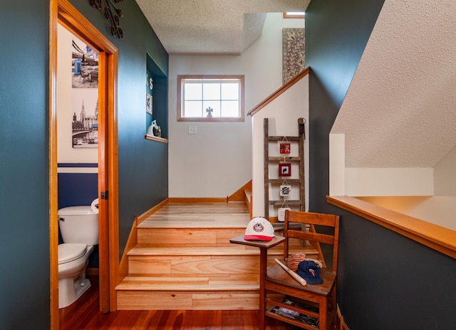 stairs featuring a textured ceiling, wood finished floors, and baseboards