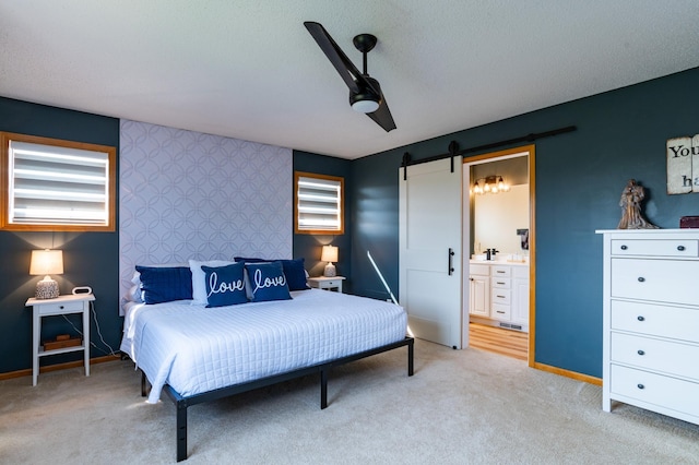 bedroom with a barn door, an accent wall, light colored carpet, baseboards, and ensuite bathroom