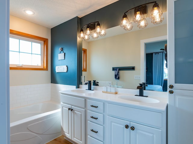 ensuite bathroom with a chandelier, double vanity, a bath, and a textured ceiling