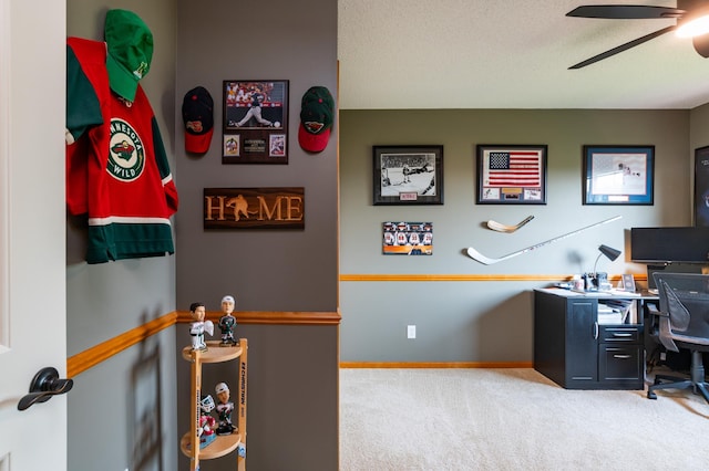 carpeted office space featuring a ceiling fan and baseboards