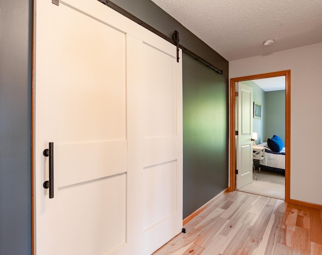hall with light wood finished floors, a barn door, a textured ceiling, and baseboards