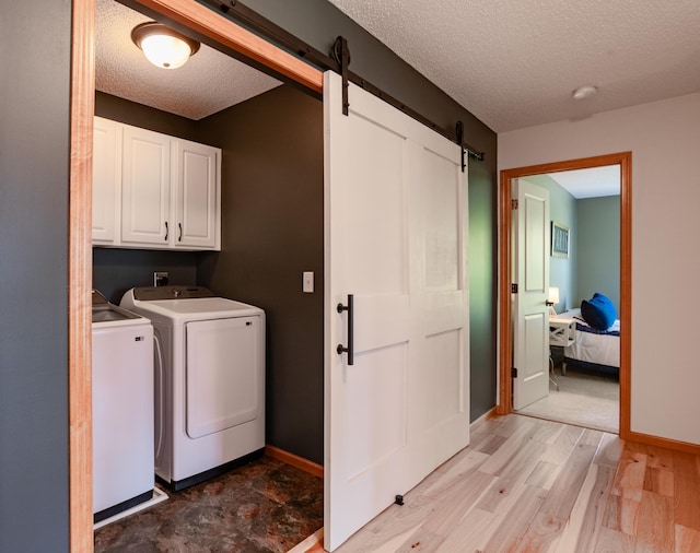 washroom featuring cabinet space, washing machine and dryer, a barn door, a textured ceiling, and light wood finished floors