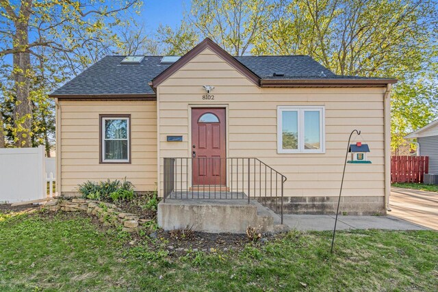 bungalow featuring a front lawn, roof with shingles, and fence