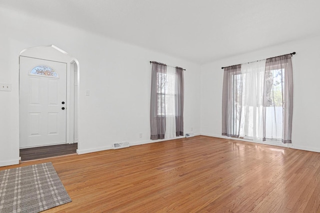 interior space featuring arched walkways, light wood-style floors, visible vents, and baseboards