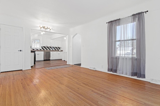 unfurnished living room featuring light wood-style flooring, arched walkways, baseboards, and visible vents