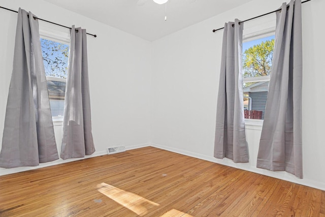 empty room with a healthy amount of sunlight, baseboards, light wood-type flooring, and visible vents