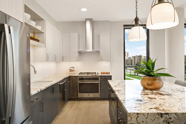 kitchen with stainless steel appliances, wall chimney range hood, a sink, open shelves, and light wood-type flooring