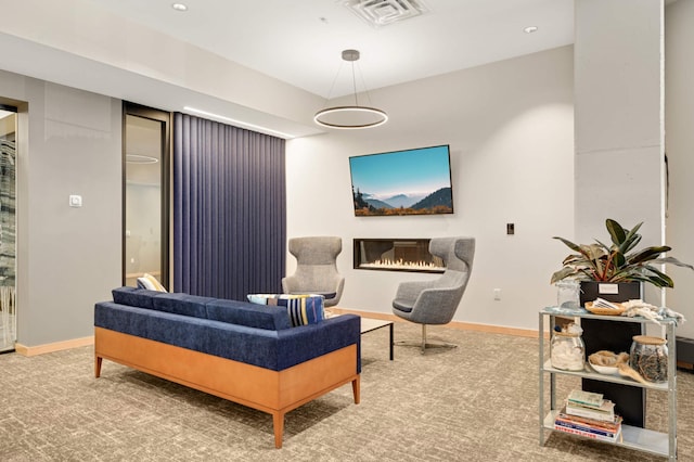 living area with a glass covered fireplace, baseboards, and carpet