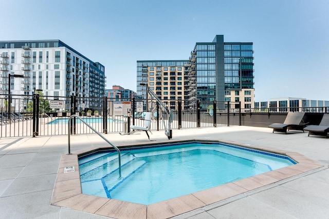 community pool with fence, a patio area, and a city view