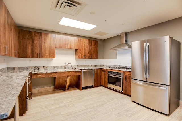 kitchen featuring stainless steel appliances, wall chimney range hood, brown cabinetry, a sink, and backsplash
