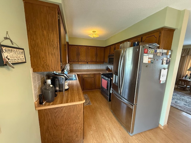 kitchen with light wood-style flooring, a textured ceiling, light countertops, tasteful backsplash, and appliances with stainless steel finishes