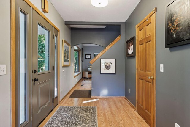 entryway featuring arched walkways, a wealth of natural light, baseboards, and wood finished floors
