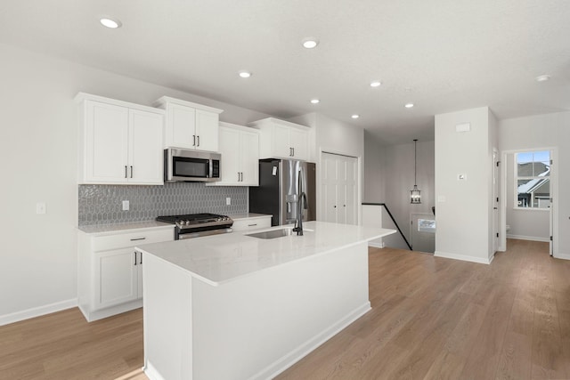 6738 Wildflower Way, Minnetrista, MN 55331 - kitchen with appliances with stainless steel finishes, a kitchen island with sink, decorative backsplash, light wood-style floors, and white cabinetry