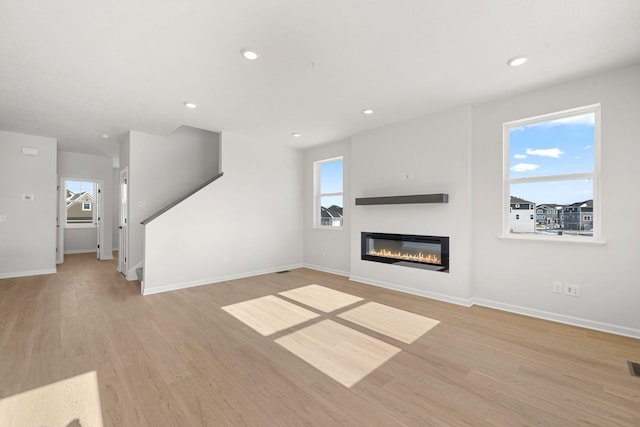 6738 Wildflower Way, Minnetrista, MN 55331 - unfurnished living room with a glass covered fireplace, baseboards, light wood-style flooring, healthy amount of natural light, and recessed lighting