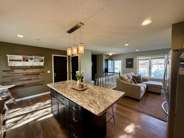 kitchen with freestanding refrigerator, a textured ceiling, dark wood-style flooring, and a kitchen bar