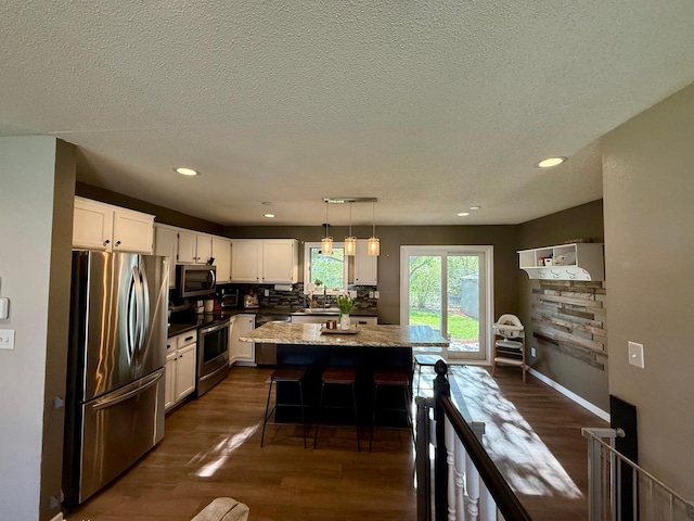 kitchen with appliances with stainless steel finishes, a kitchen island, dark wood-style floors, and white cabinetry