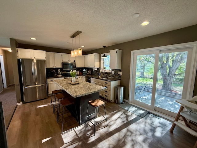 kitchen with a sink, dark wood-type flooring, appliances with stainless steel finishes, a kitchen island, and tasteful backsplash