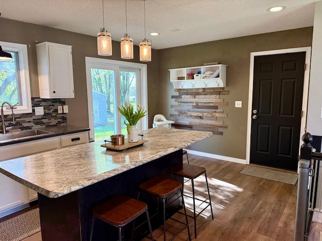 kitchen with a kitchen bar, a sink, dark wood finished floors, white cabinetry, and backsplash