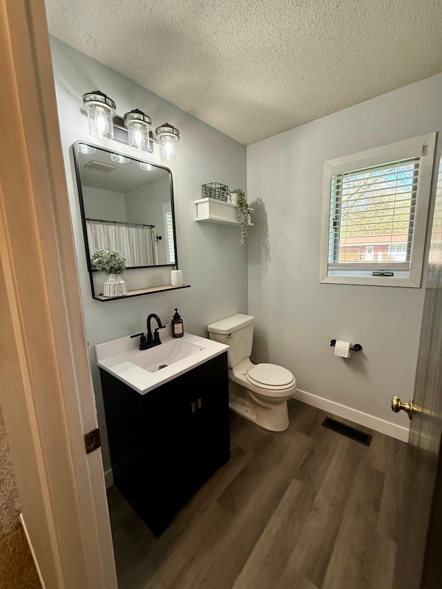 bathroom with a textured ceiling, toilet, visible vents, vanity, and wood finished floors