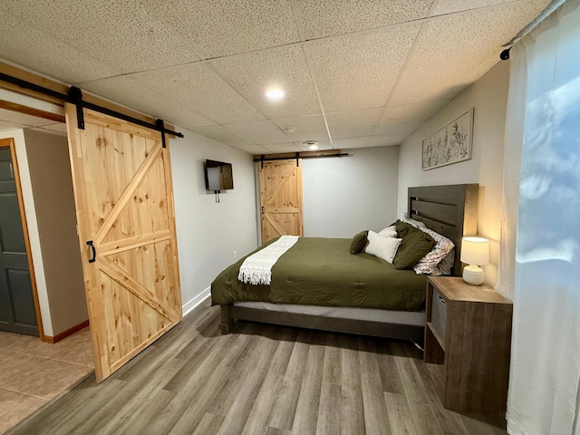bedroom featuring a paneled ceiling, a barn door, baseboards, and wood finished floors