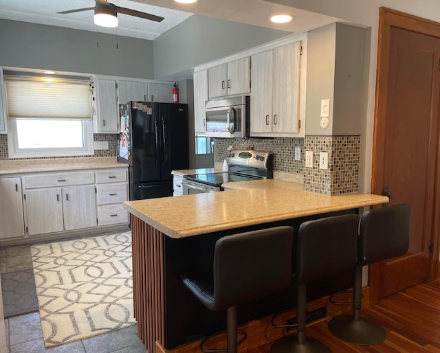 kitchen with a peninsula, a ceiling fan, stainless steel appliances, light countertops, and tasteful backsplash