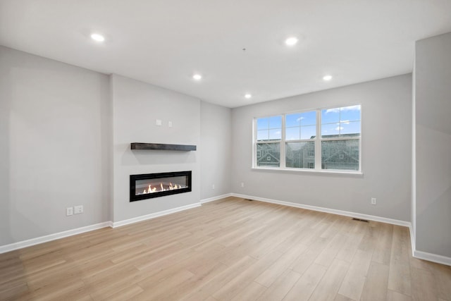 6754 Wildflower Way, Minnetrista, MN 55331 - unfurnished living room featuring light wood-style flooring, a glass covered fireplace, baseboards, and recessed lighting