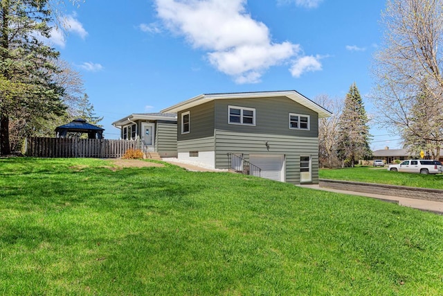 rear view of property featuring a garage, fence, a lawn, concrete driveway, and a gazebo