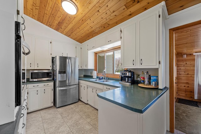 kitchen featuring a sink, a peninsula, vaulted ceiling, dark countertops, and appliances with stainless steel finishes