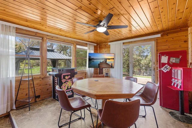 dining space with wooden ceiling, wooden walls, a ceiling fan, and stone finish floor