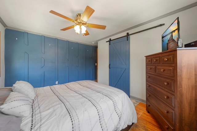bedroom with crown molding, a barn door, a ceiling fan, and wood finished floors