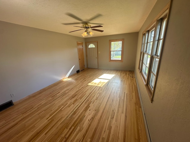 unfurnished living room with light wood finished floors, baseboards, a textured ceiling, and a ceiling fan